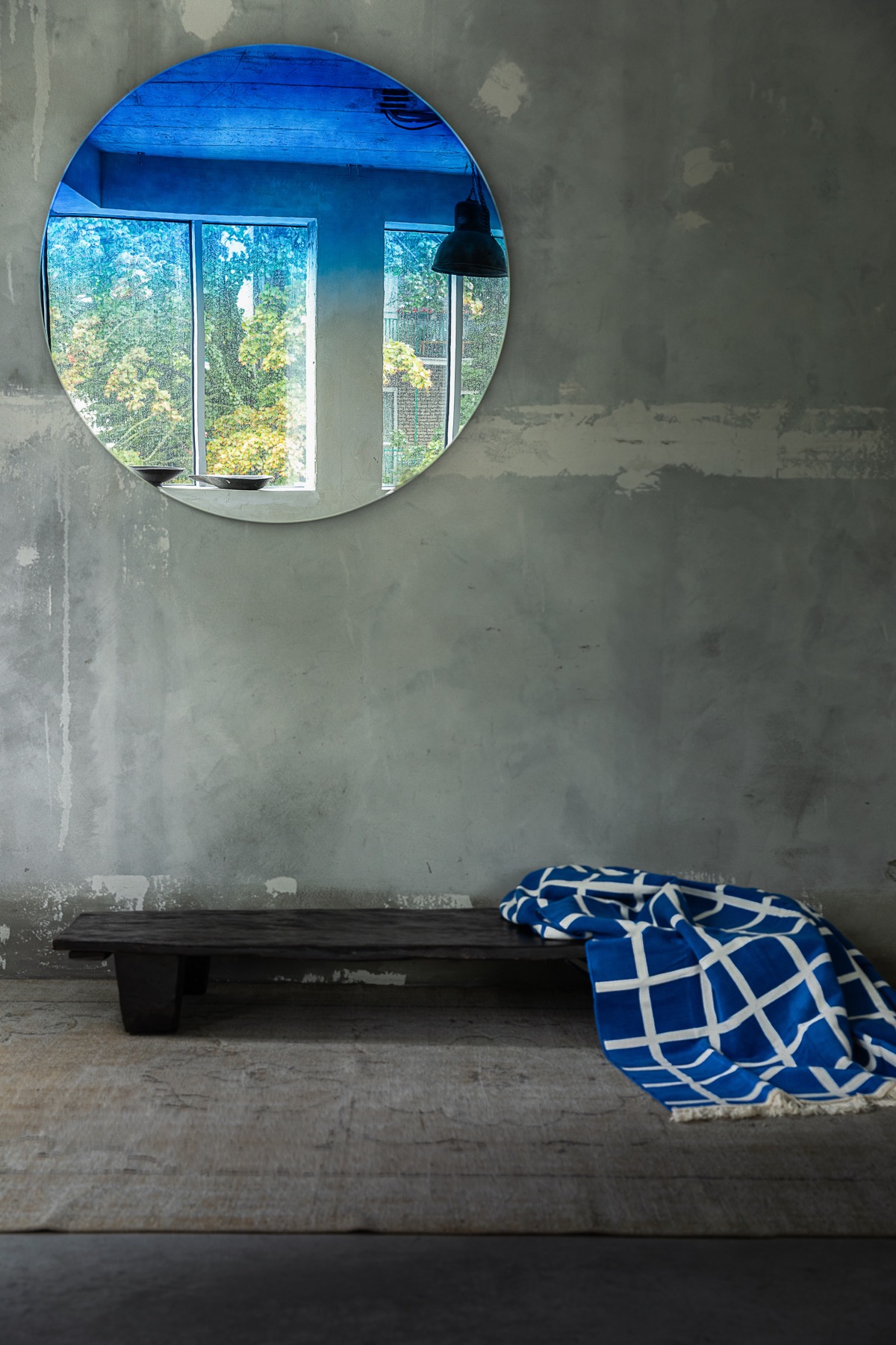 The Neptune mirror on a concrete wall above a low bench with a blue blanket