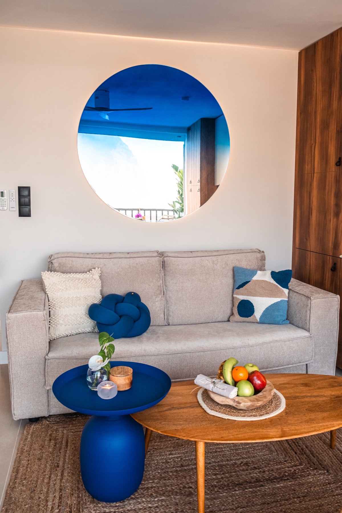 The Neptune mirror with a deep cobalt gradient hanging above a sofa in a sunlit hotel suite
